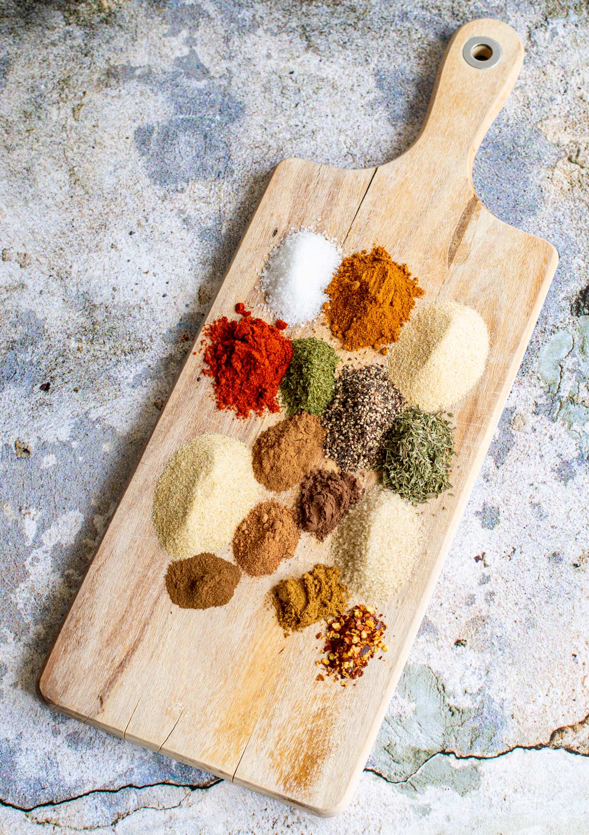 piles of spices on a wooden chopping board sat on a chipped stone bench top