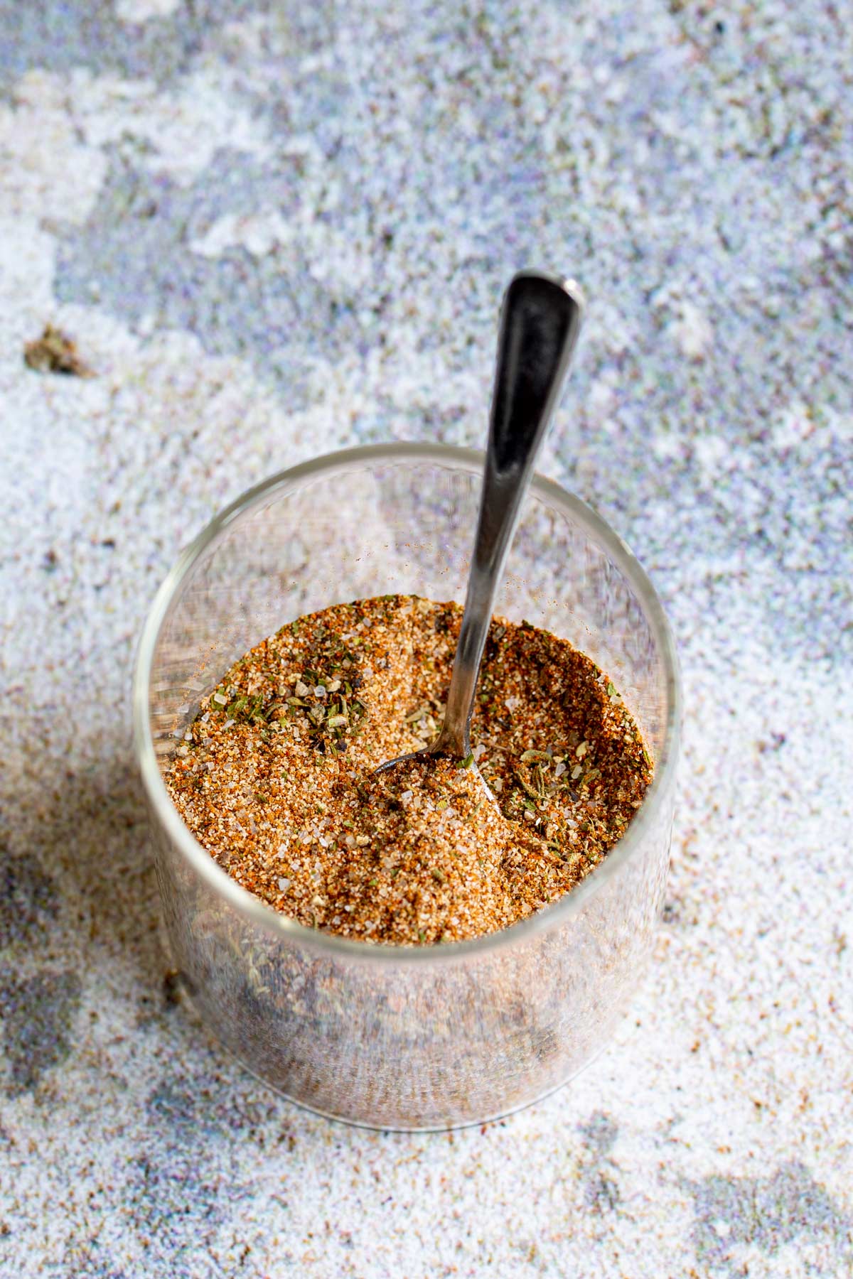 a glass jar of seasoning blend with a spoon in it on a stone slab