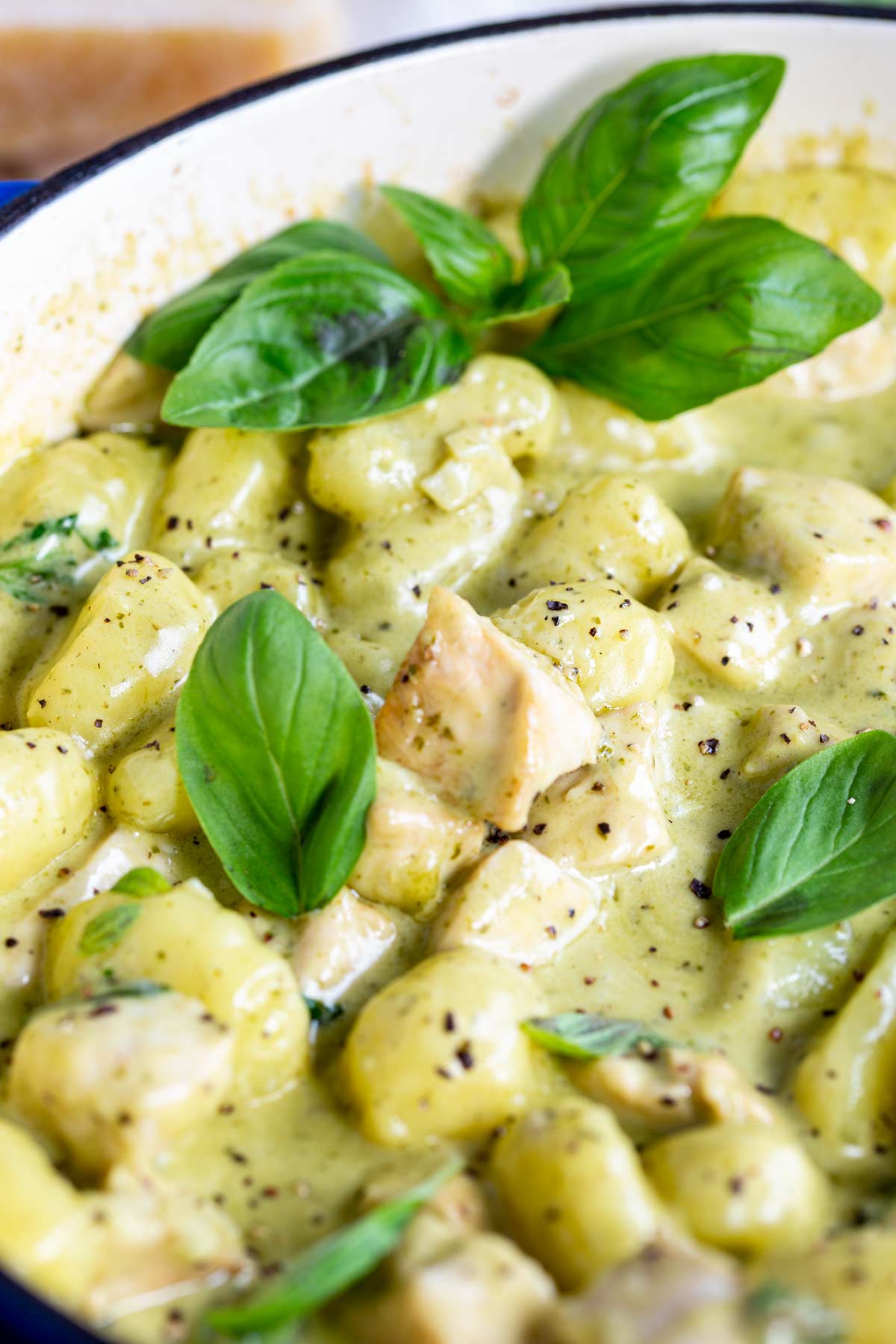 close up on the chunks of chicken in a pan of creamy pesto gnocchi