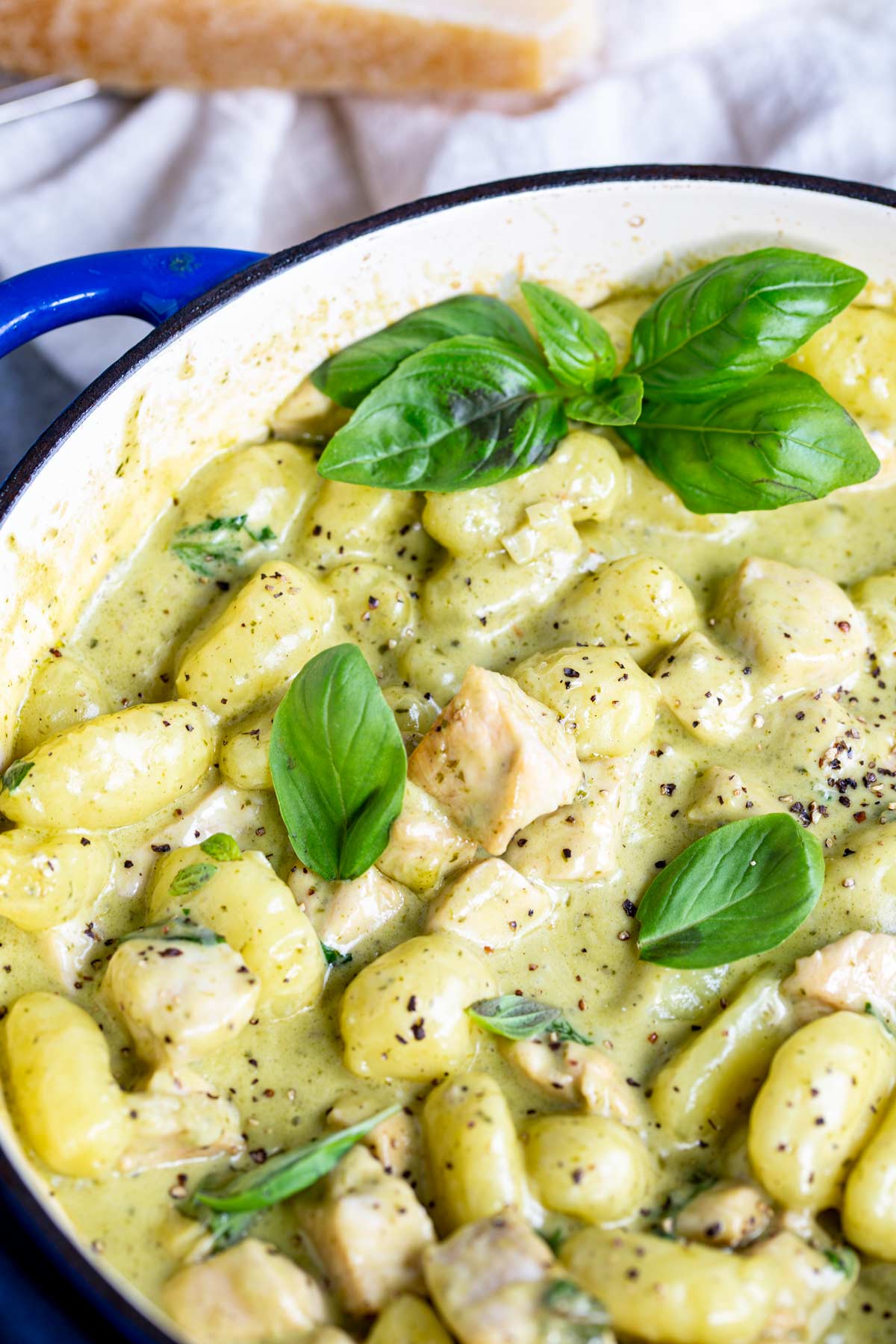 gnocchi in a creamy basil sauce with fresh basil on top in a blue pan