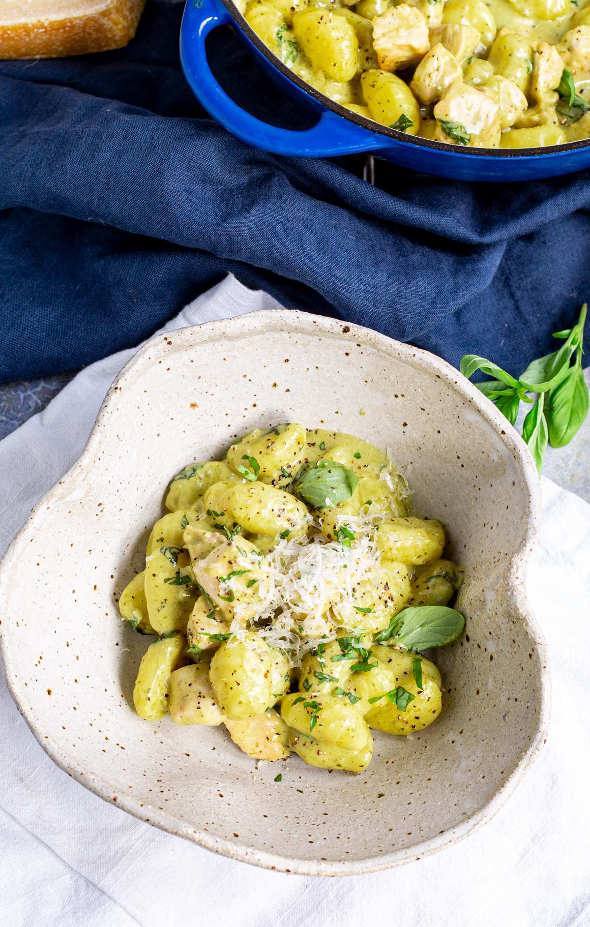 a rustic bowl of pesto gnocchi with a blue pan in the background