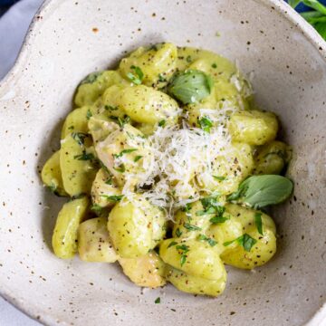 a rustic bowl of gnocchi in a creamy green sauce with grated parmesan on top
