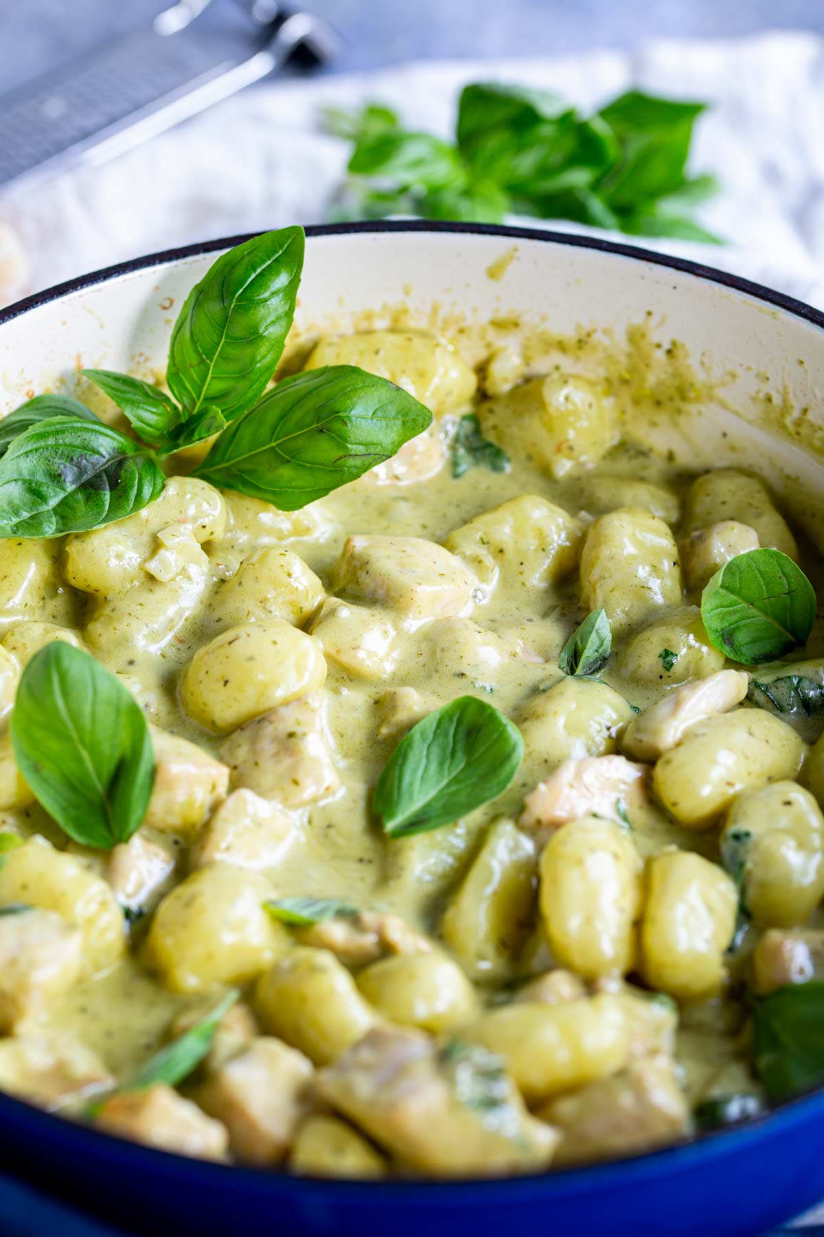 a blue cast iron skillet with creamy pesto gnocchi in it, garnished with basil leaves