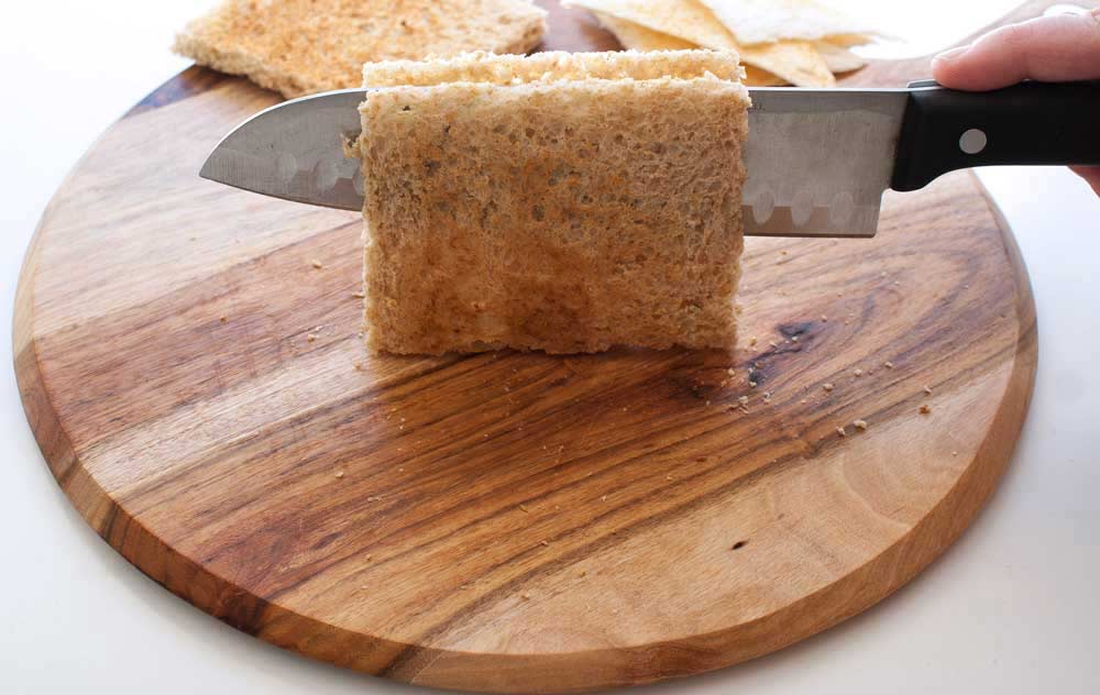a  sharp knife cutting through the middle of a piece of toast on a wooden board