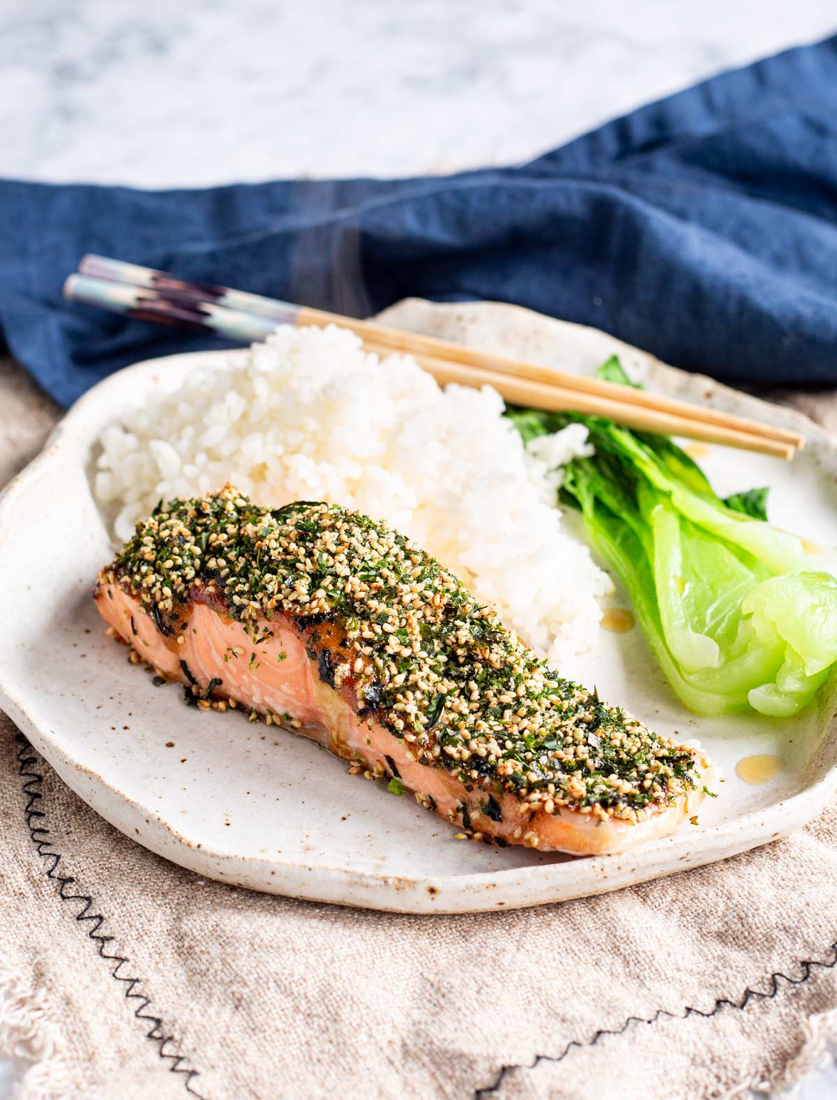 a salmon fillet with a crispy seaweed top, on a rustic plate with rice and greens