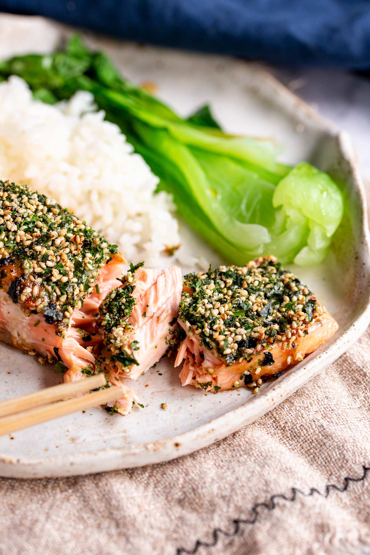 chop sticks breaking off some flakes of salmon from a fillet coated in Furikake