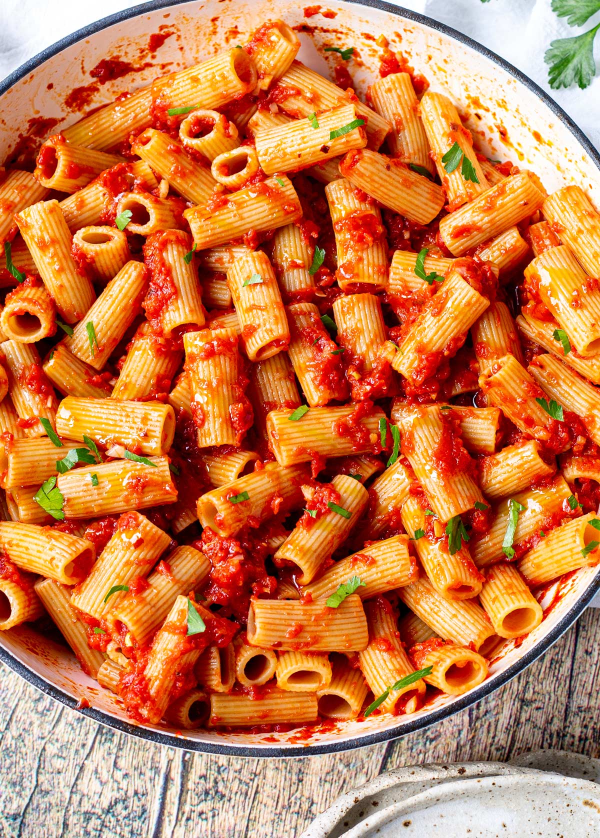 overhead of rigatoni arrabbiata in a large shallow pan with a pile of rustic plates
