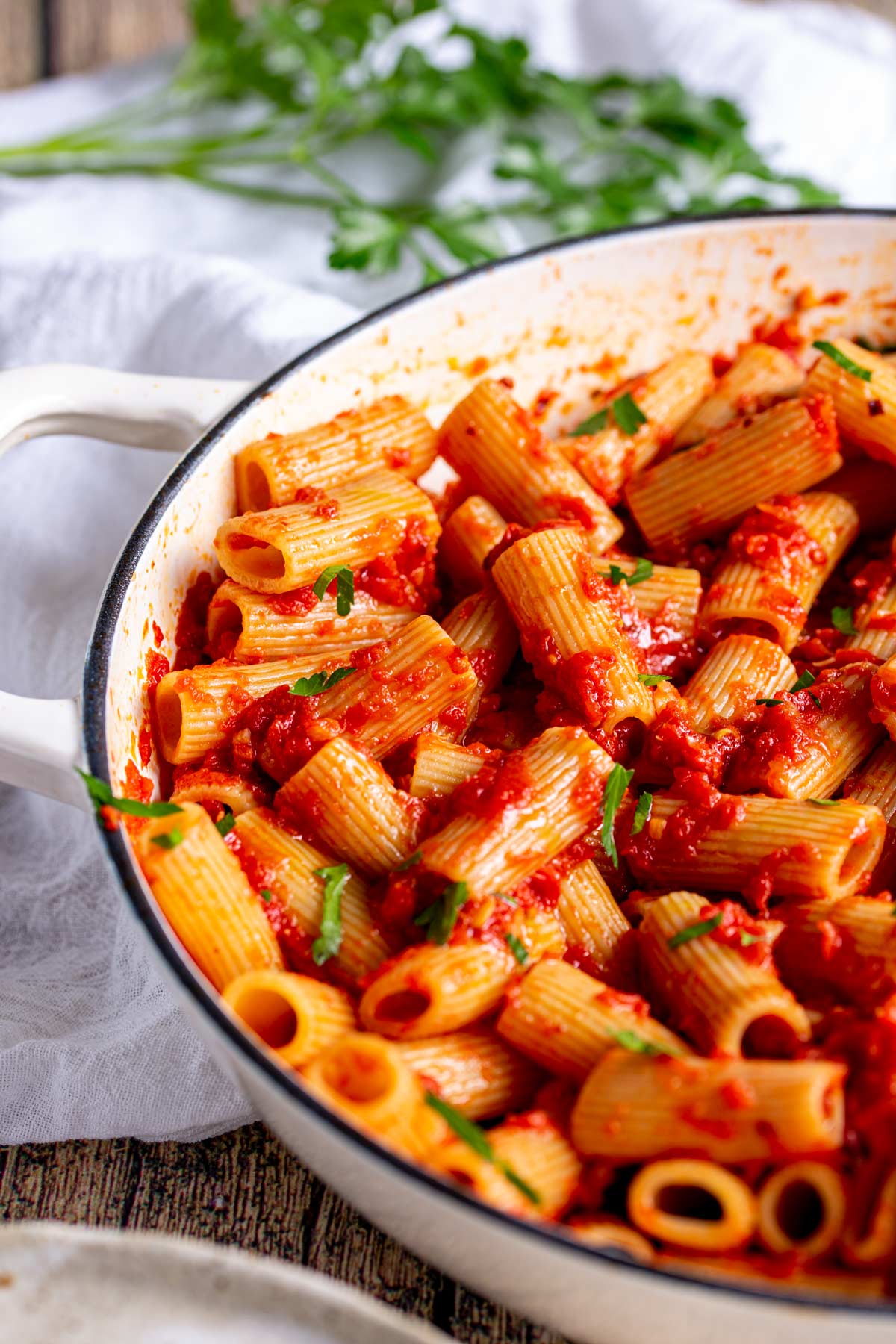 a shallow cream cast iron dish filled with tomato rigatoni with a napkin underneath