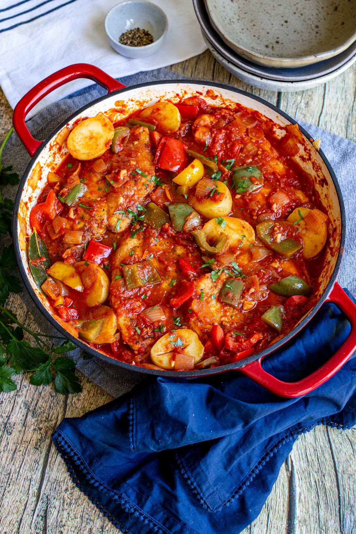 a red cast iron pan filled with tomato, chicken, potatoes and bell peppers