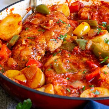 close up on two chicken breasts in a pan with tomato, potato and bell peppers