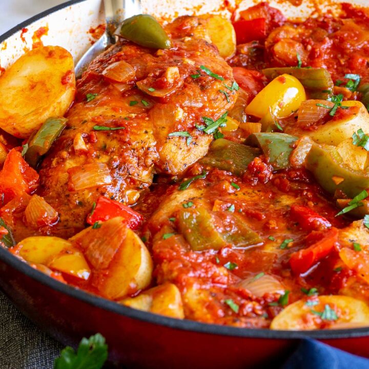 close up on two chicken breasts in a pan with tomato, potato and bell peppers