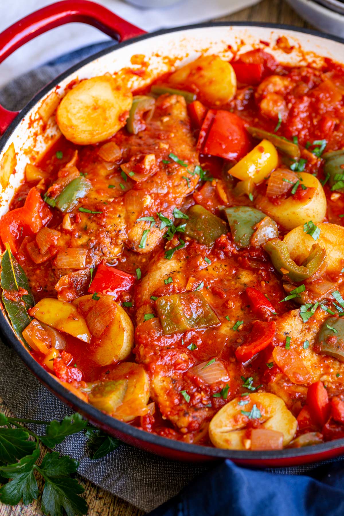 chicken breasts and potatoes in a cast iron pan in a tomato sauce garnished with parsley