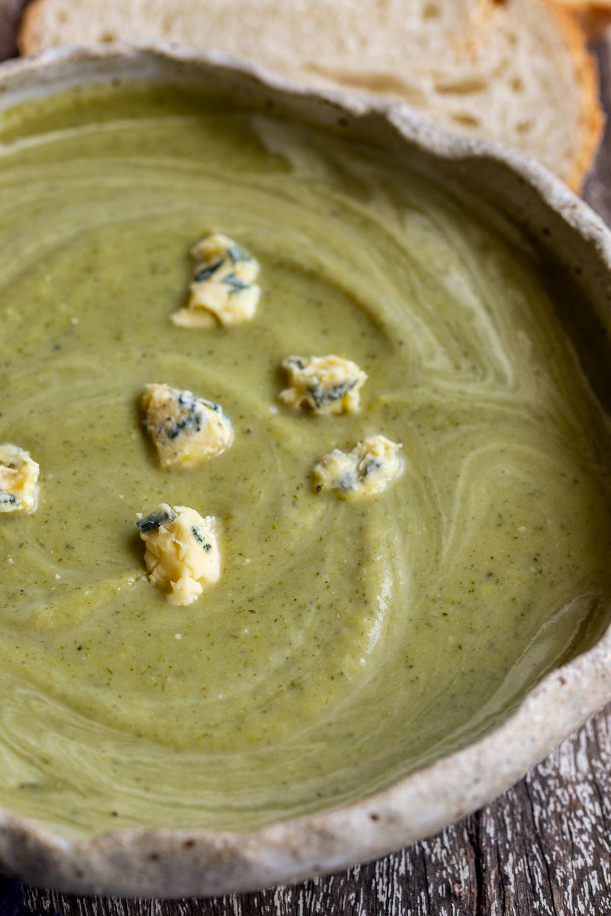 close up on chunks of blue cheese in a bowl of green broccoli soup