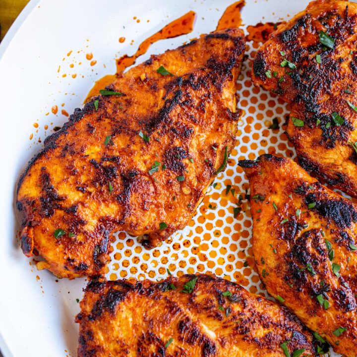 close up on a white frying pan with cooked harissa marinated chicken breasts in it