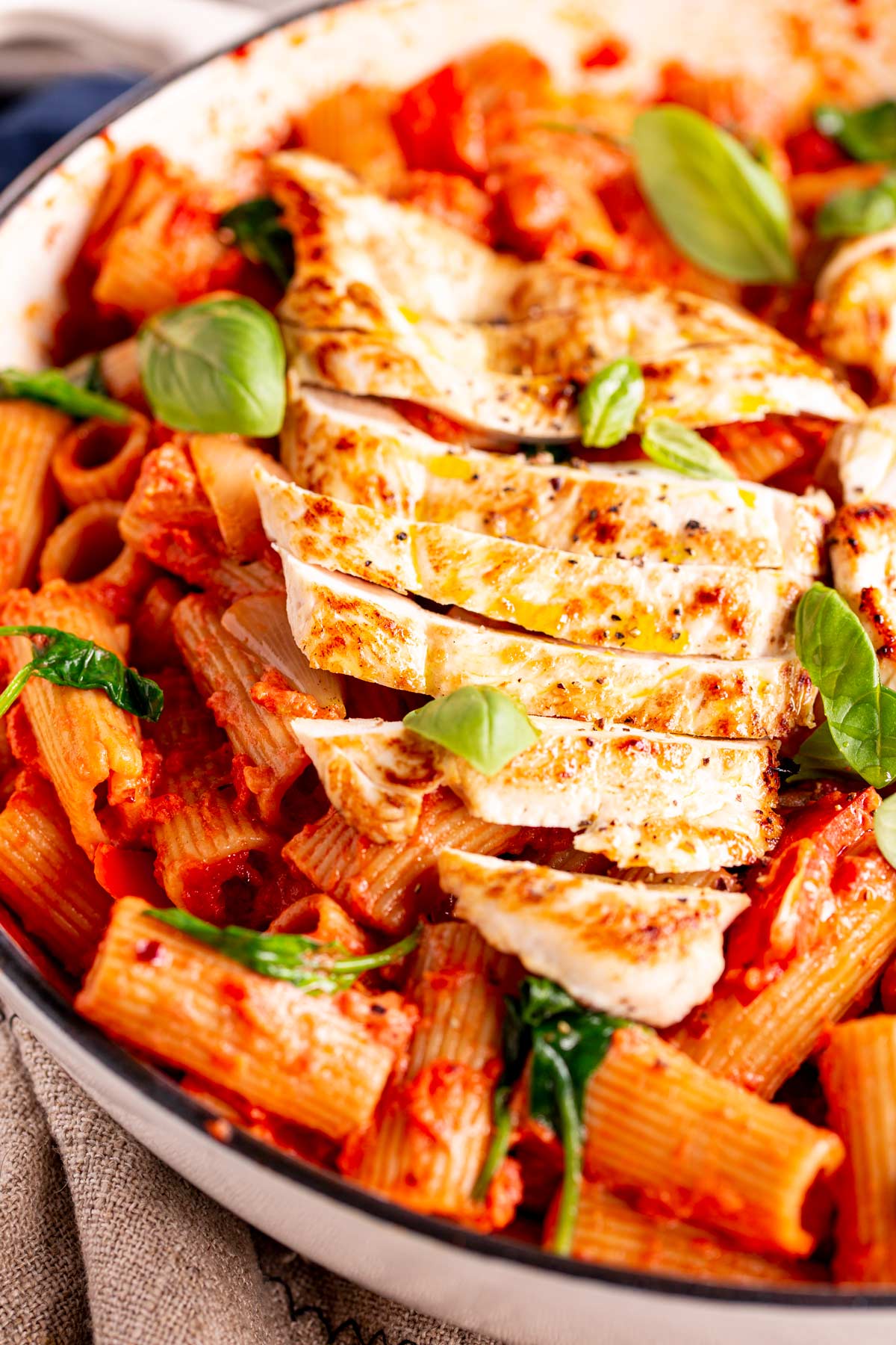 close up on the sliced chicken in a pan of tomato pasta with fresh basil leaves