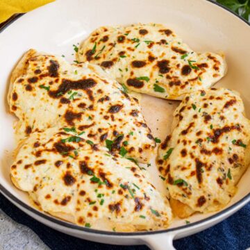 close up on 4 cheese topped chicken breasts in a cast iron skillet