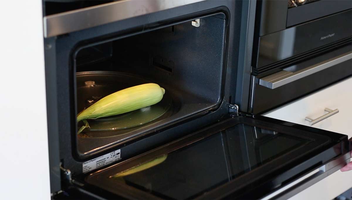 a corn on the cob with the husk still on, sitting in a microwave