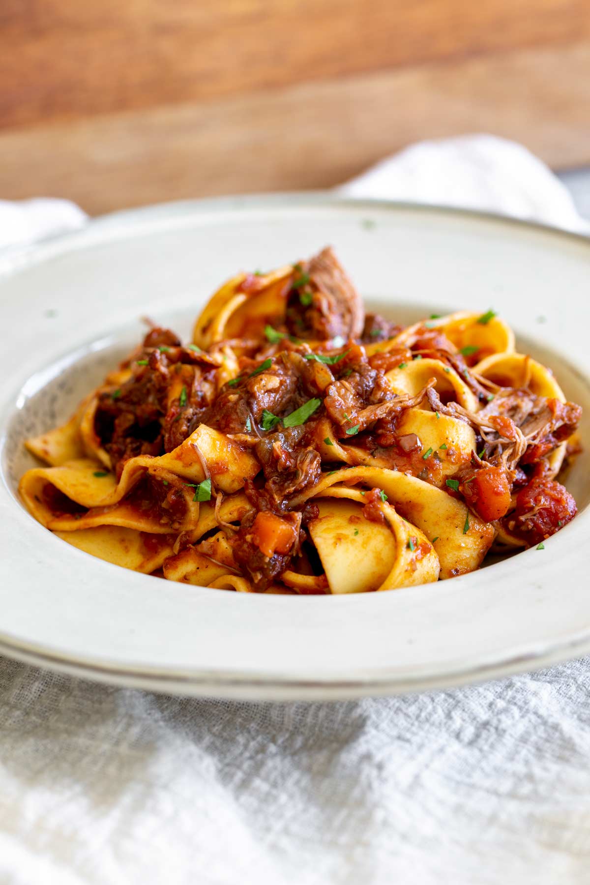 a rustic wide bowl with thick pasta and shredded meat sauce on a linen napkin
