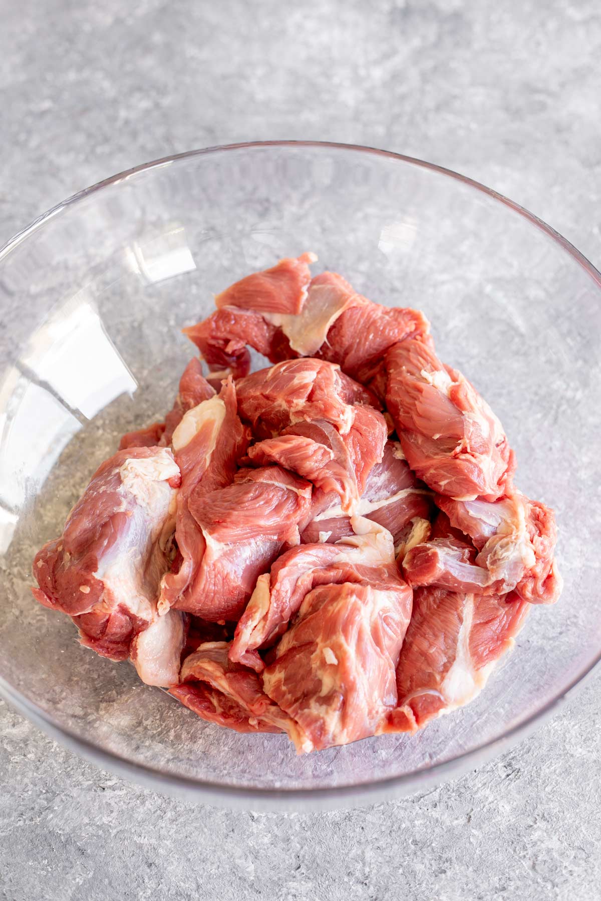 large chunks of raw lamb in a glass bowl on a stone table