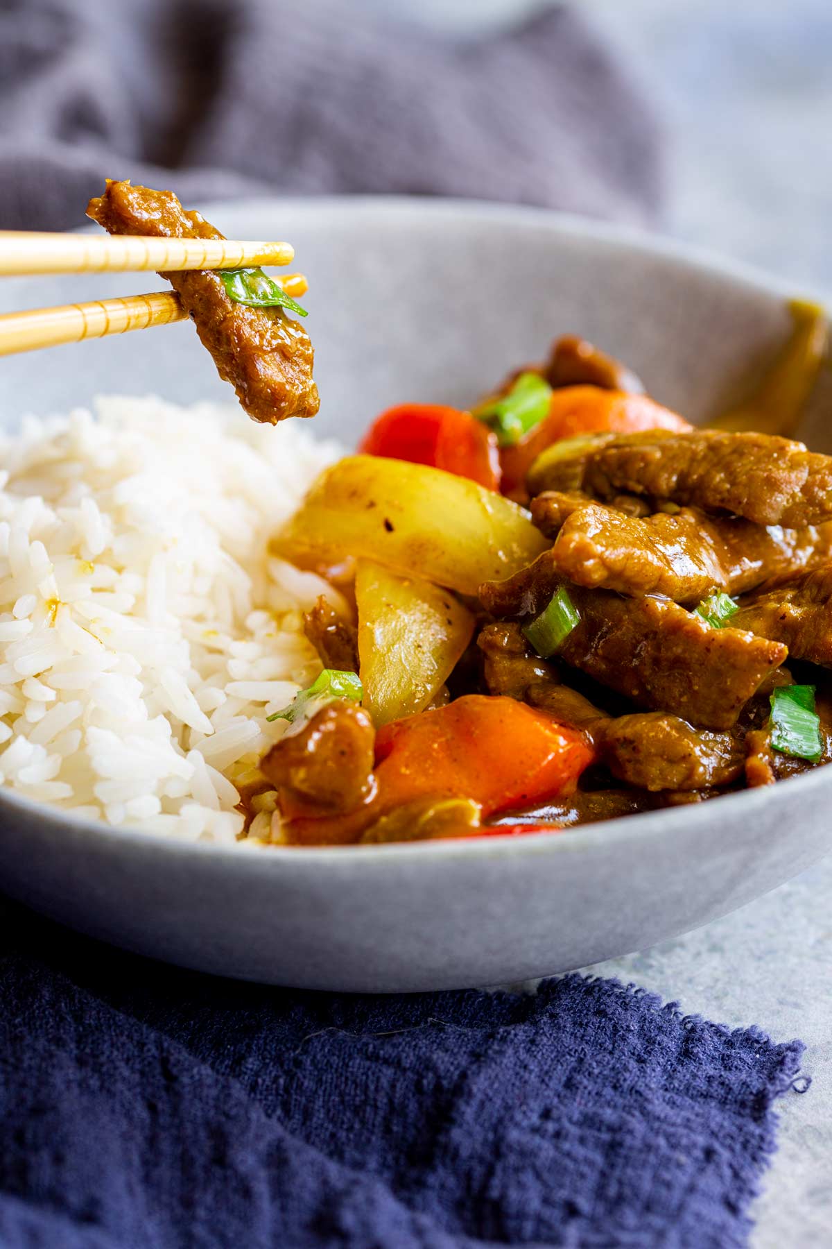 chopsticks holding a piece of beef over a bowl of beef in sauce with veg and rice