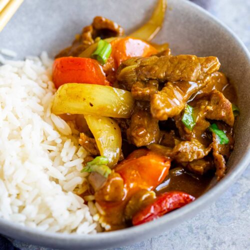 super close up of some strips of beef in curry sauce with a grey bowl with rice