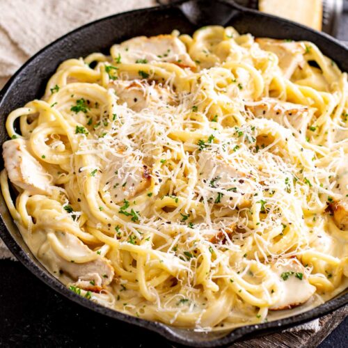 a cast iron pan of chicken and pasta in aa creamy sauce garnished with parsley