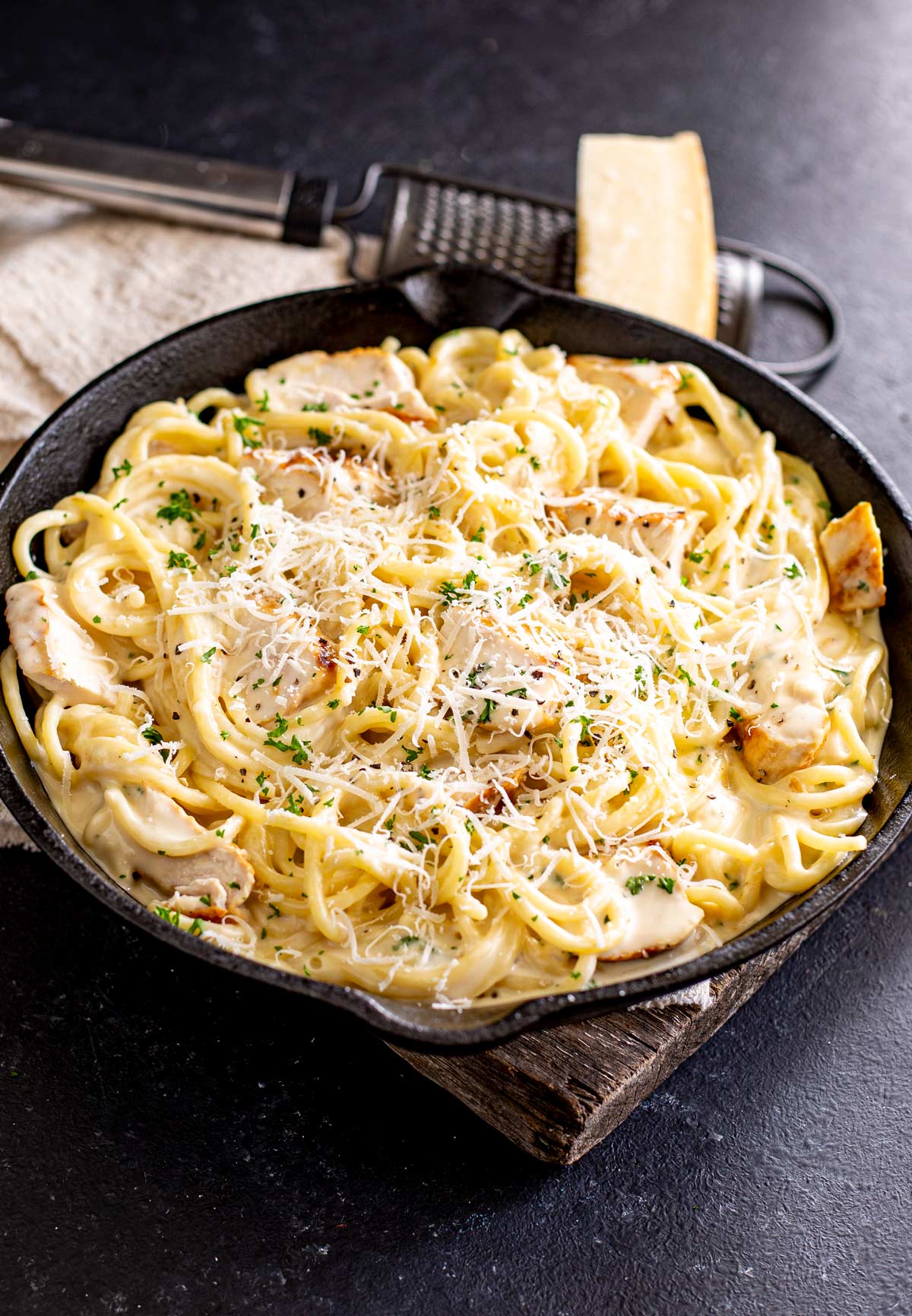 a skillet of creamy pasta on a wooden board with parmesan and a grater behind