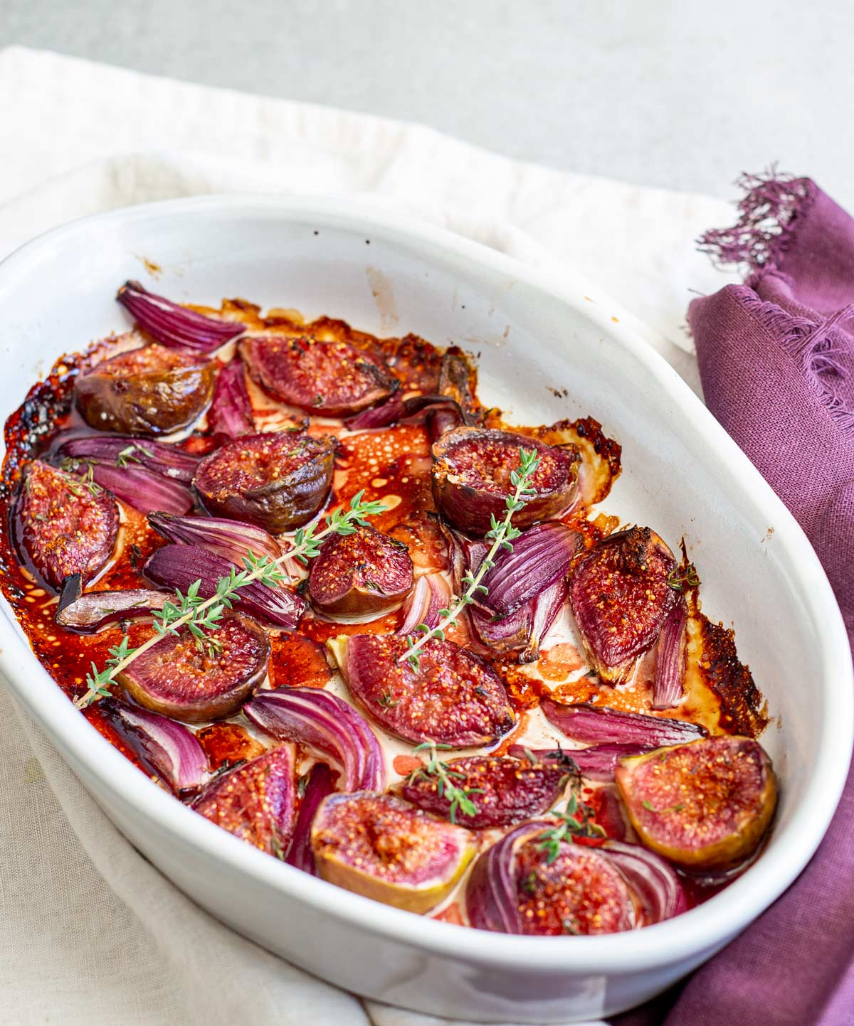 a oval baking dish filled with roasted figs and onion on a linen napkin