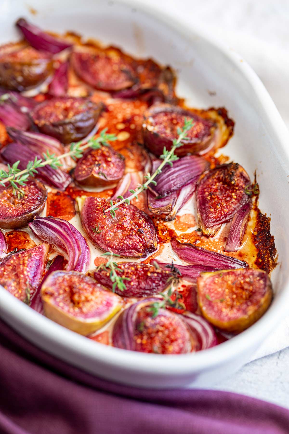 a white baking dish filled with baked fig and red onion with thyme