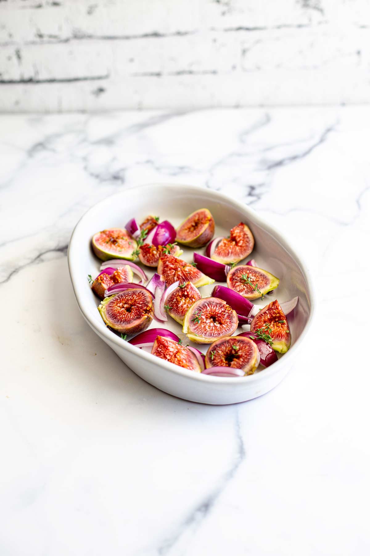 a white oval dish filled with fresh figs halves and red onion slices