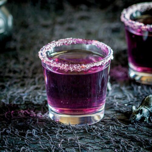Close up of a purple cocktail in a shot glass with sugar rim