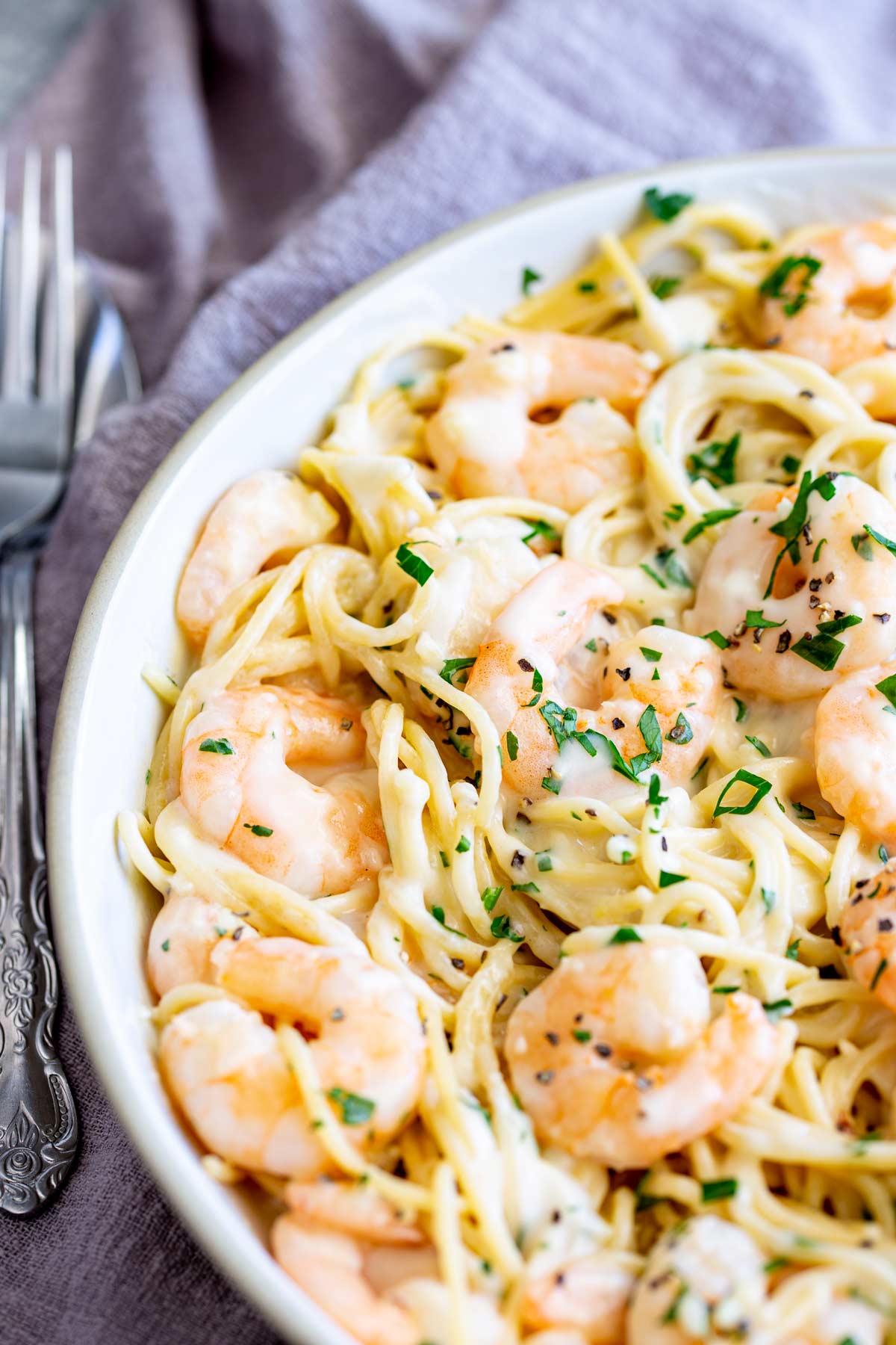 a fork next to a bowl of creamy shrimp spaghetti with parsley garnish
