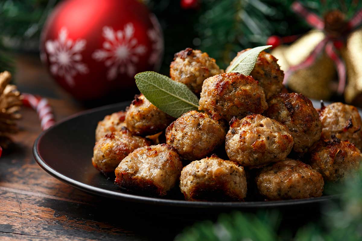 stuffing balls on a black plate garnished with sage, with Christmas baubles behind