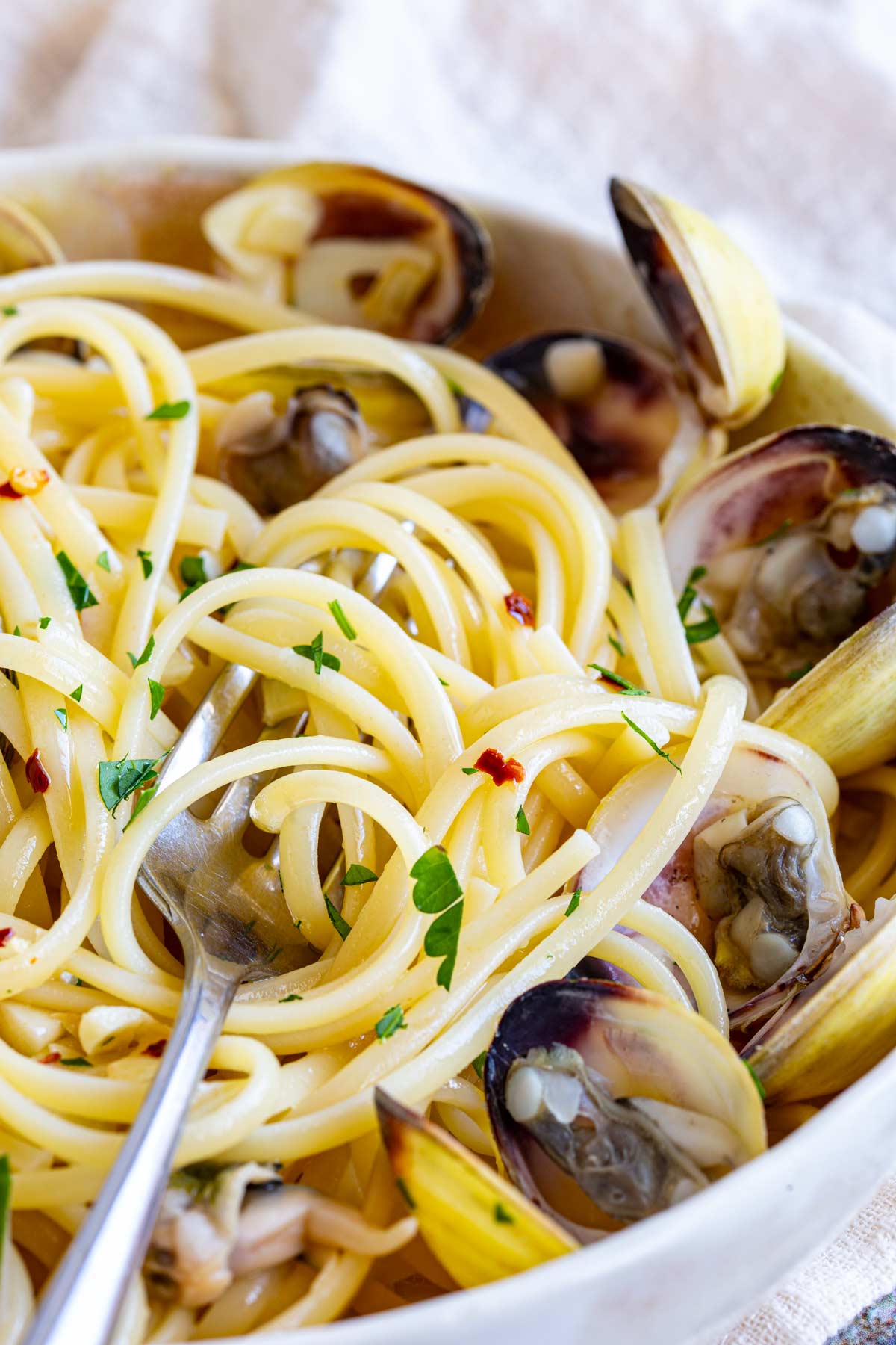 a fork swirling up pasta from a bowl of clams and linguine with garlic, chili and parsley