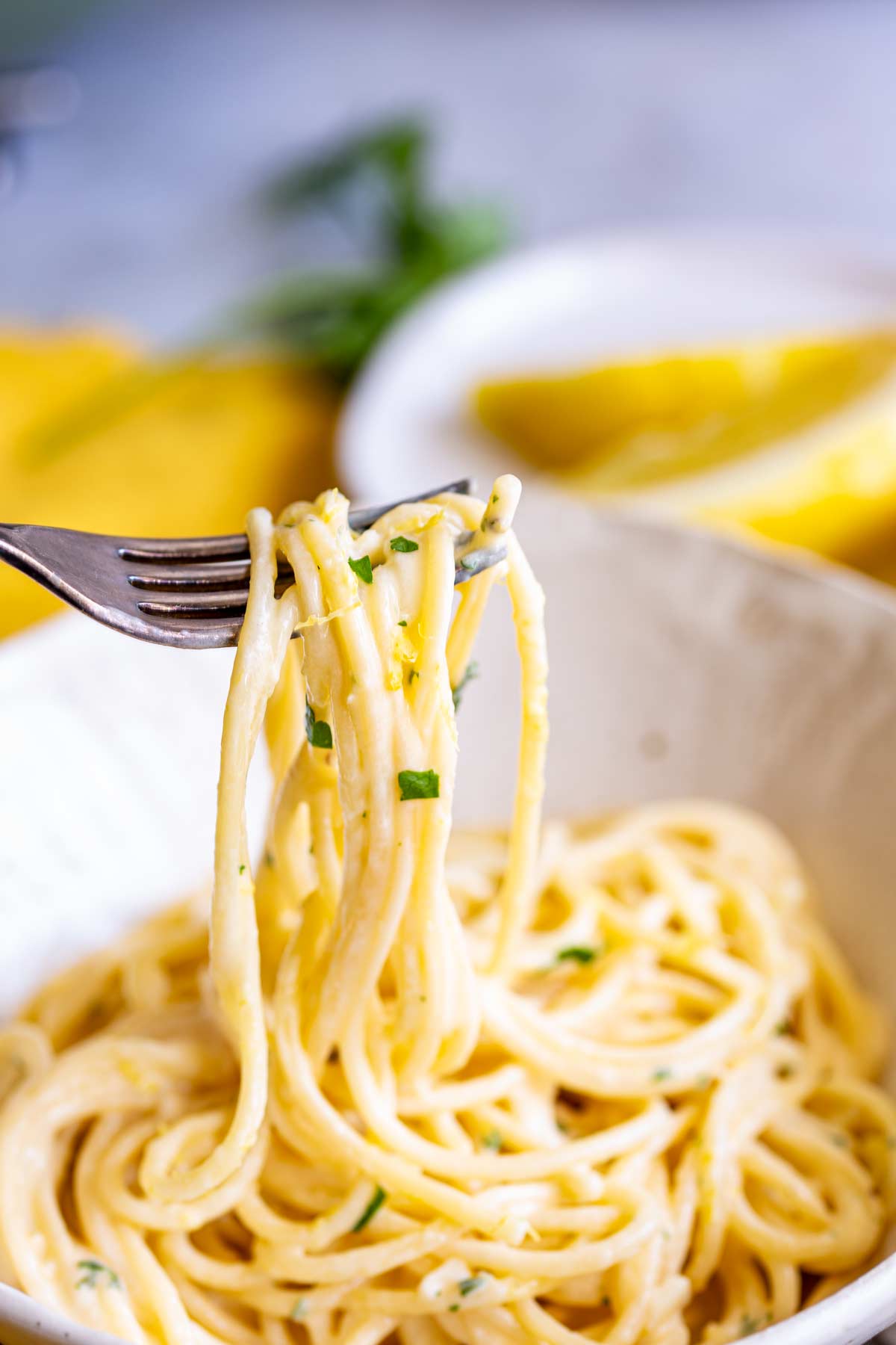 a fork picking up some creamy spaghetti from a white bowl