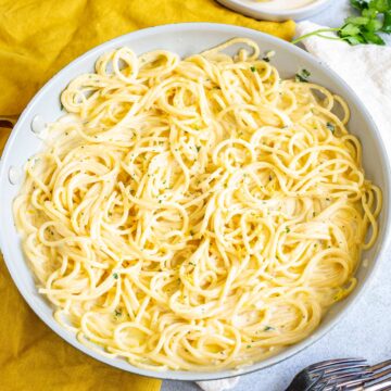 skillet of spaghetti in a creamy lemon sauce with a yellow napkin