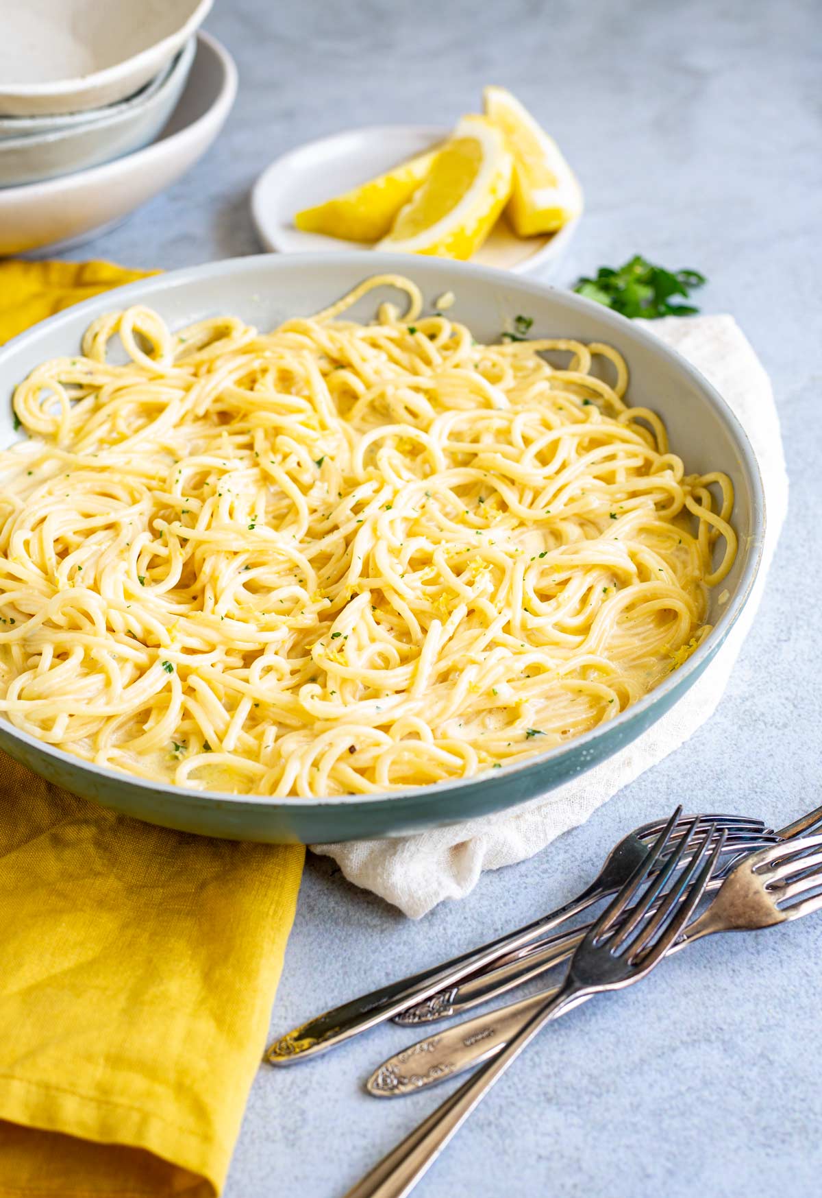 frying pan filled with pasta on a stone table with lemon wedges and rustic forks