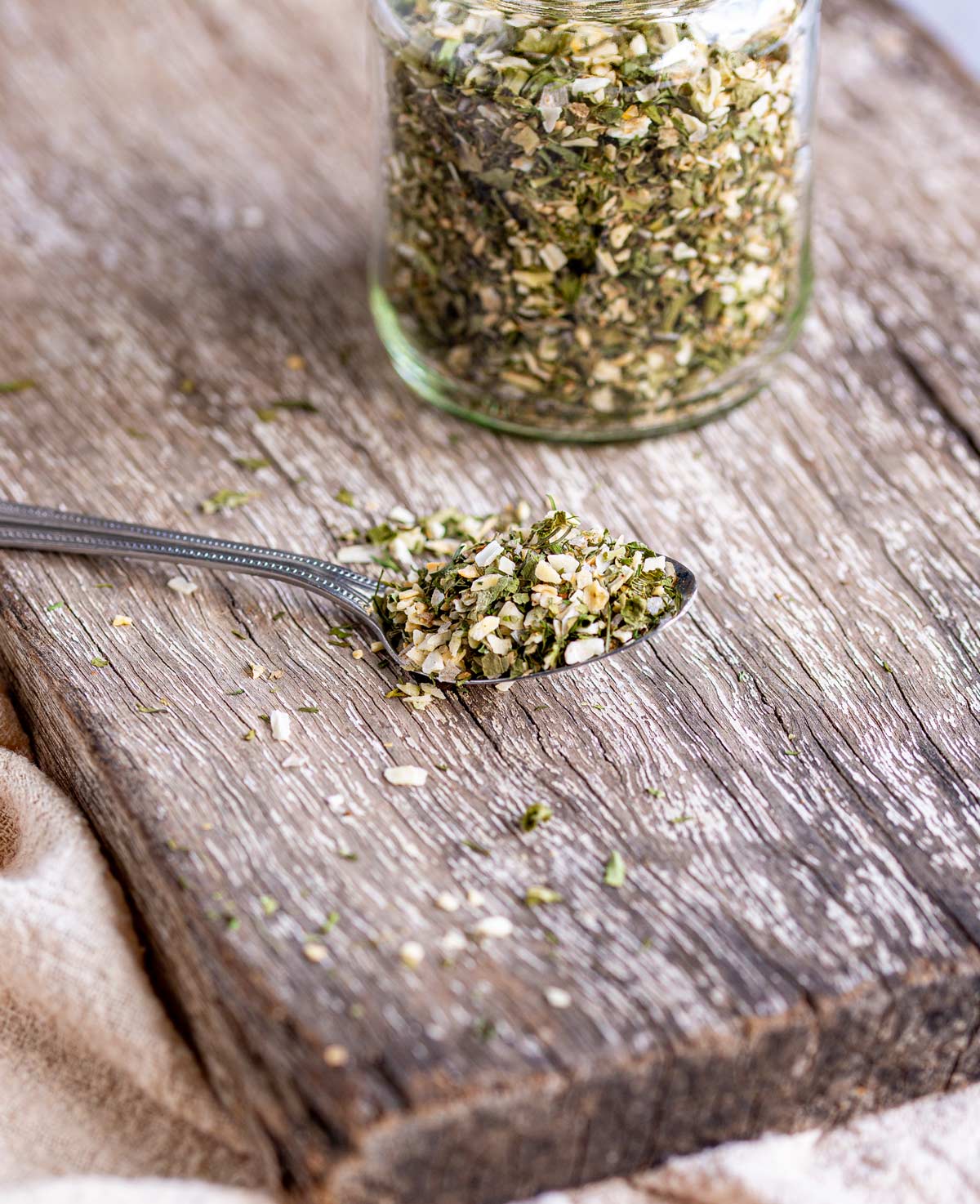 a spoon with herbs on it, on a wooden board with a jar in the background