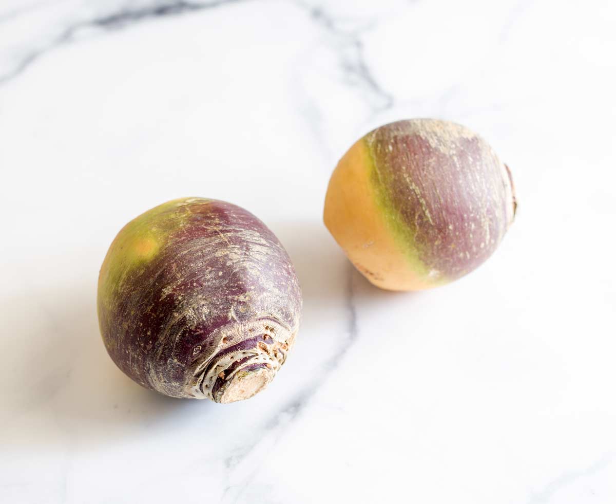 two unpeeled rutabaga on a marble counter