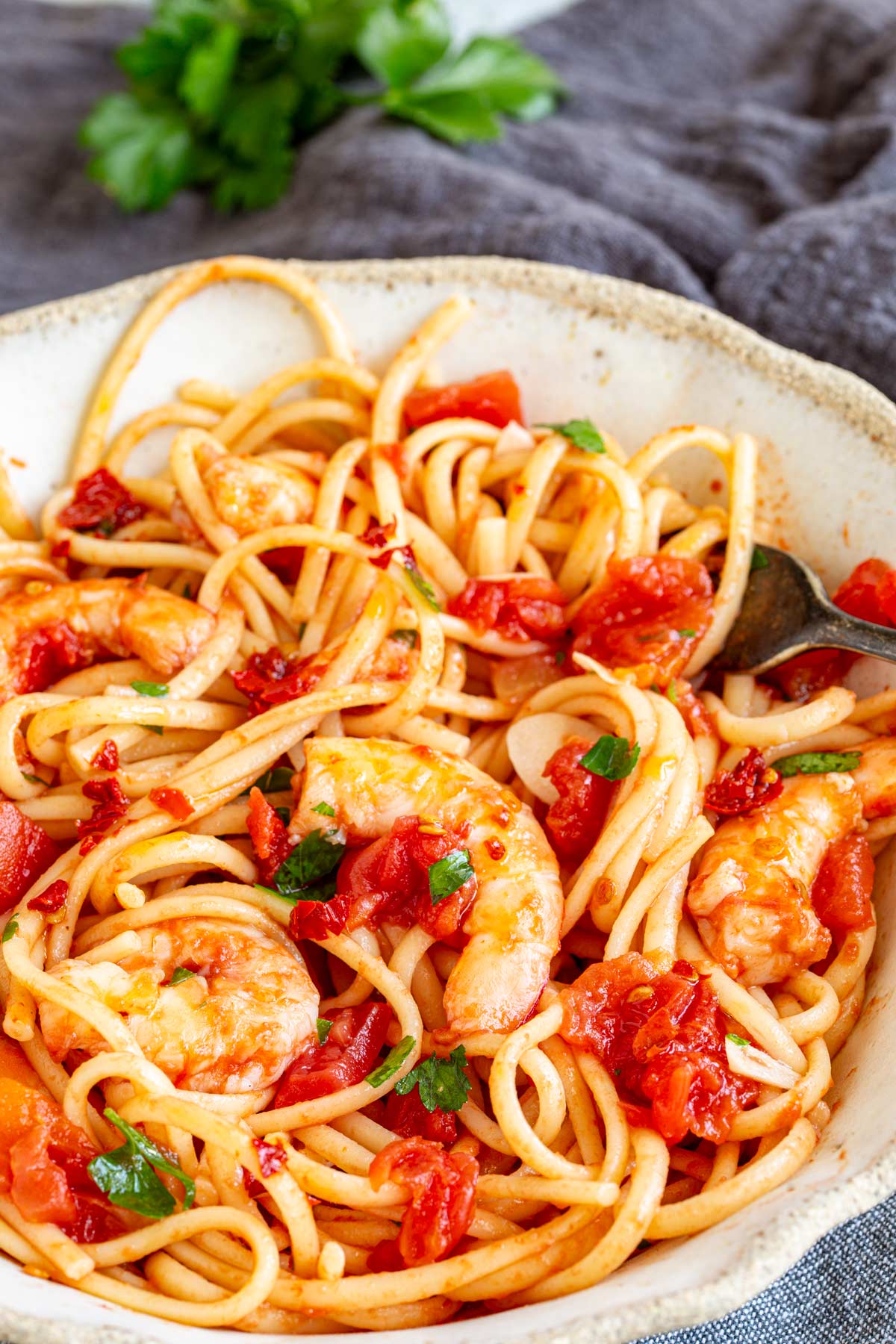 a rustic bowl filled with tomato pasta with shrimp on a grey napkin