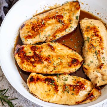 4 cooked chicken fillets in a white skillet with a brown sauce
