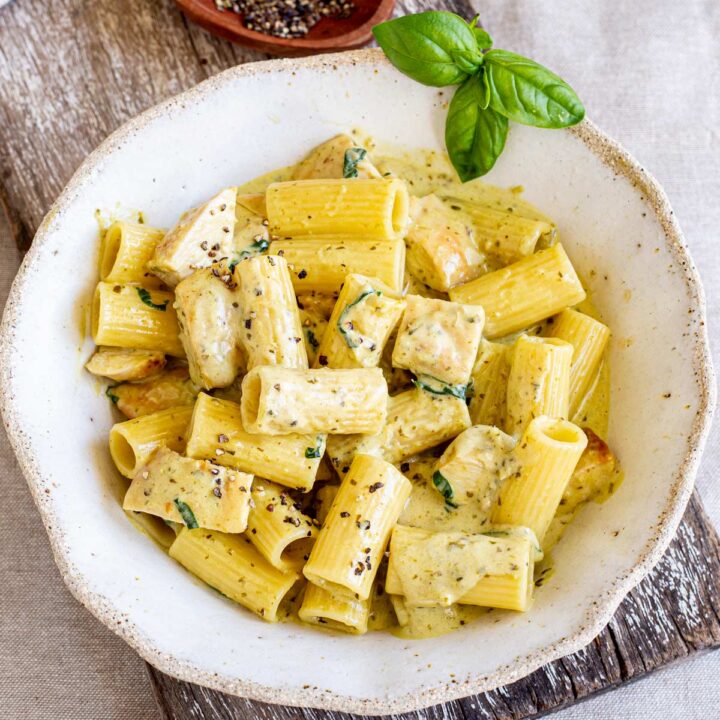 Creamy chicken pesto pasta in a white bowl, featuring sliced chicken, penne pasta coated in a creamy pesto sauce, and garnished with fresh basil and cracked black pepper.