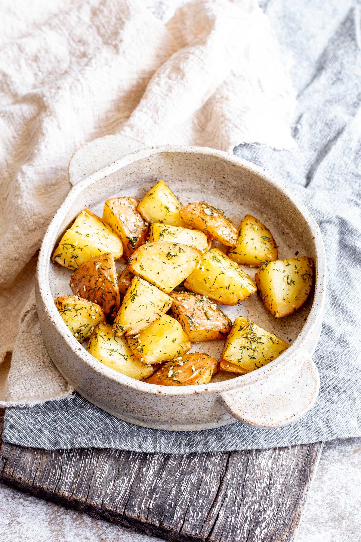 a wooden board with linen napkins and a rustic round dish of potatoes with dill