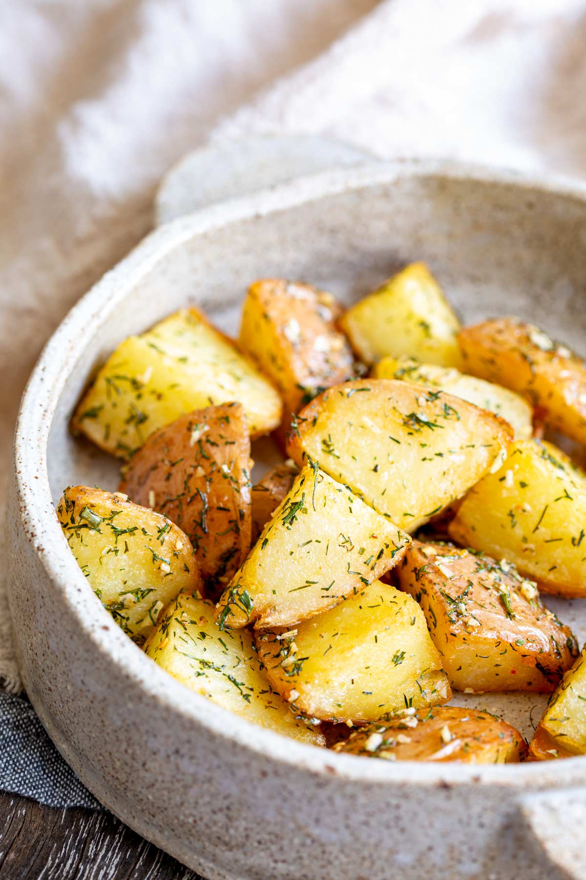 chunks of roasted potatoes with dill on them in a stoneware dish