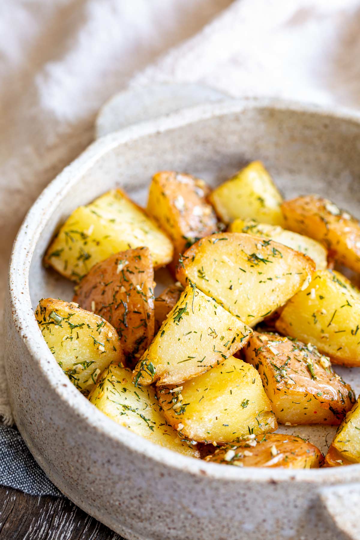 chunks of roasted potatoes with dill on them in a stoneware dish