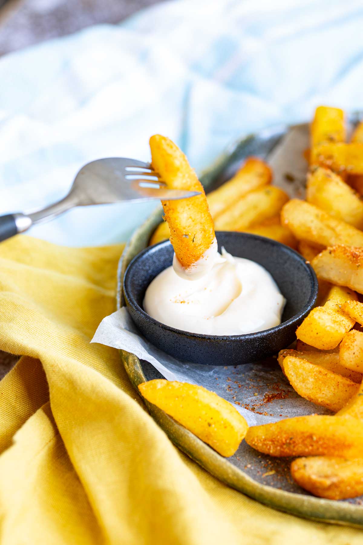 a fork dipping a French fry into a black pot of mayonnaise