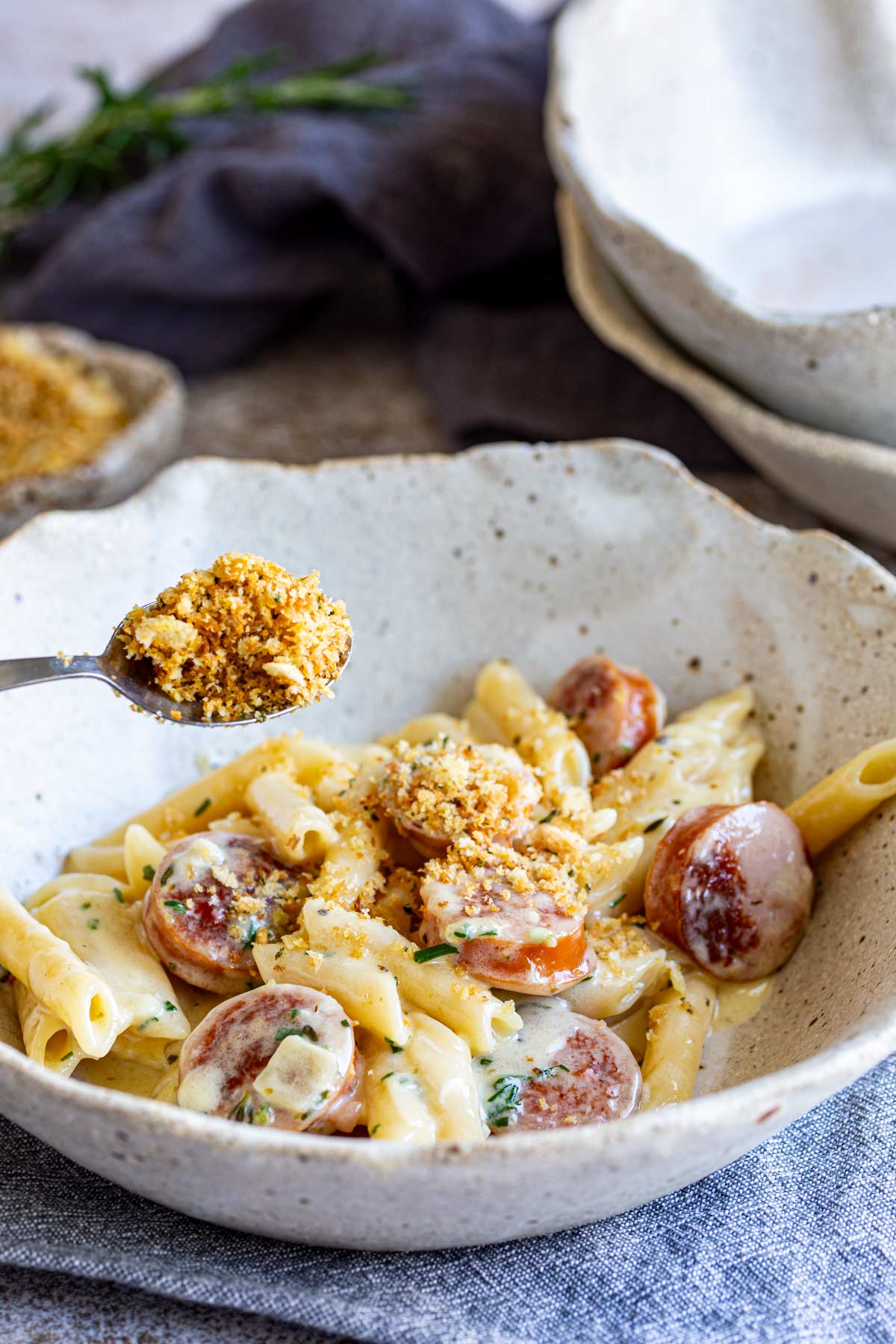 a spoon sprinkling pangrattato over a bowl of creamy pasta