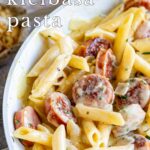 pin image: Creamy cheesy kielbasa pasta in a white skillet with text overlaid