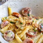 pin image: Creamy cheesy kielbasa pasta in a rustic bowl with text overlaid