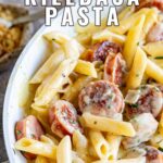 pin image: Creamy cheesy kielbasa pasta in a white skillet with text overlaid